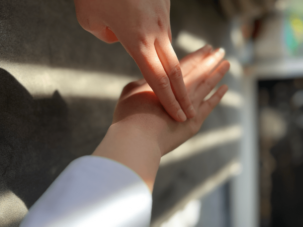 A close-up image of a hand gently tapping or pressing against another hand, creating a moment of mindfulness in a well-lit environment. EFT tapping.