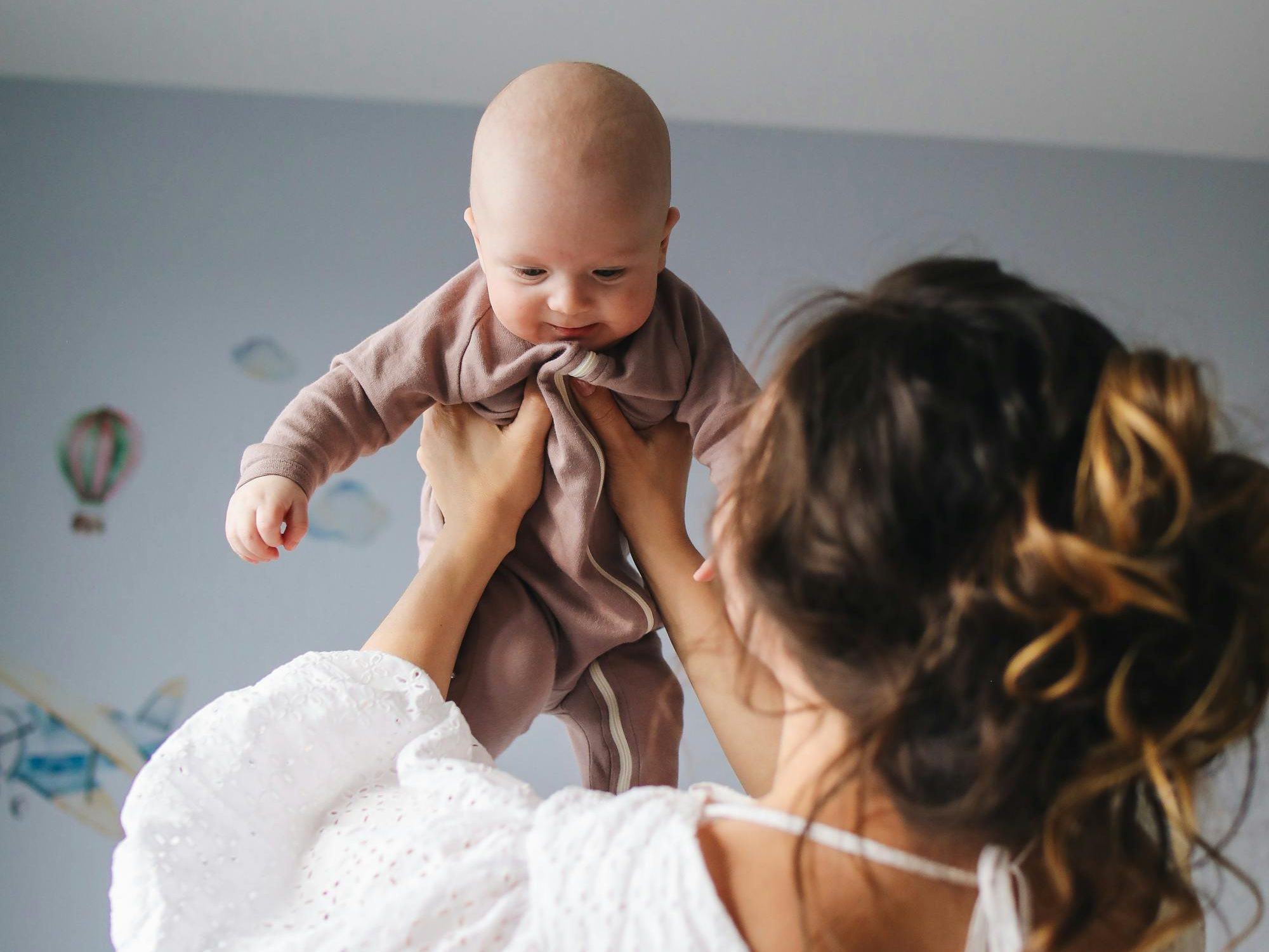 A caregiver holds up a smiling baby in a cozy indoor setting, showcasing a moment of bonding and joy.