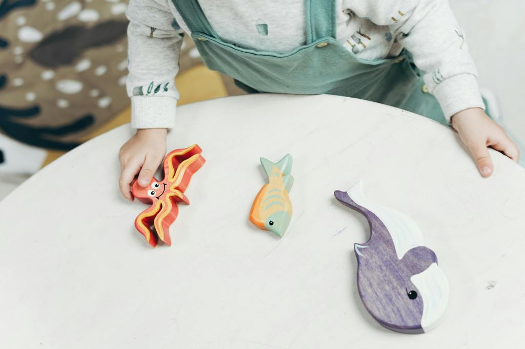 A child playing with colorful wooden sea animal toys on a table.