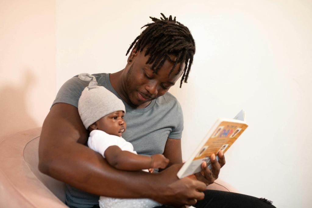 A father reading a book to his baby, both looking engaged and connected, sitting in a cozy setting.