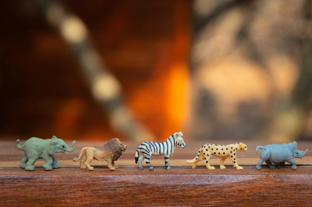 A row of five colorful animal figurines including an elephant, lion, zebra, cheetah, and rhinoceros, displayed on a wooden surface.