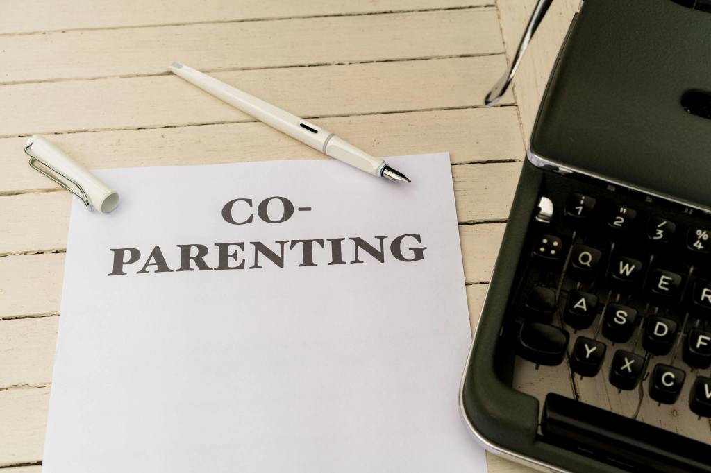 A sheet of paper titled 'CO-PARENTING' is placed on a wooden surface, accompanied by a pen and a typewriter, symbolizing the concept of shared parenting responsibilities.